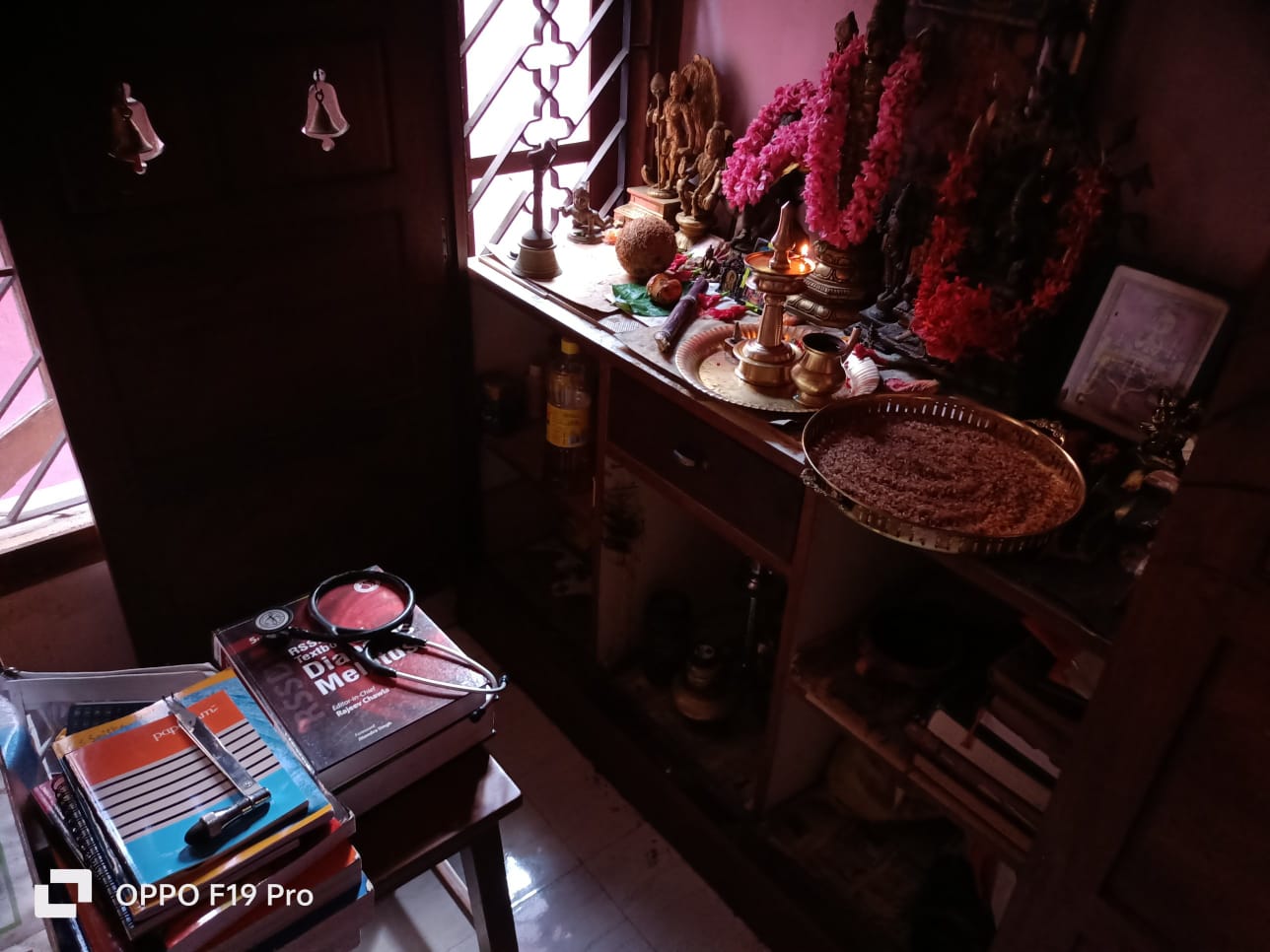 Navaratri pooja corner at home with a lit brass lamp, flowers and idols, and books, a pen and instruments kept for pooja