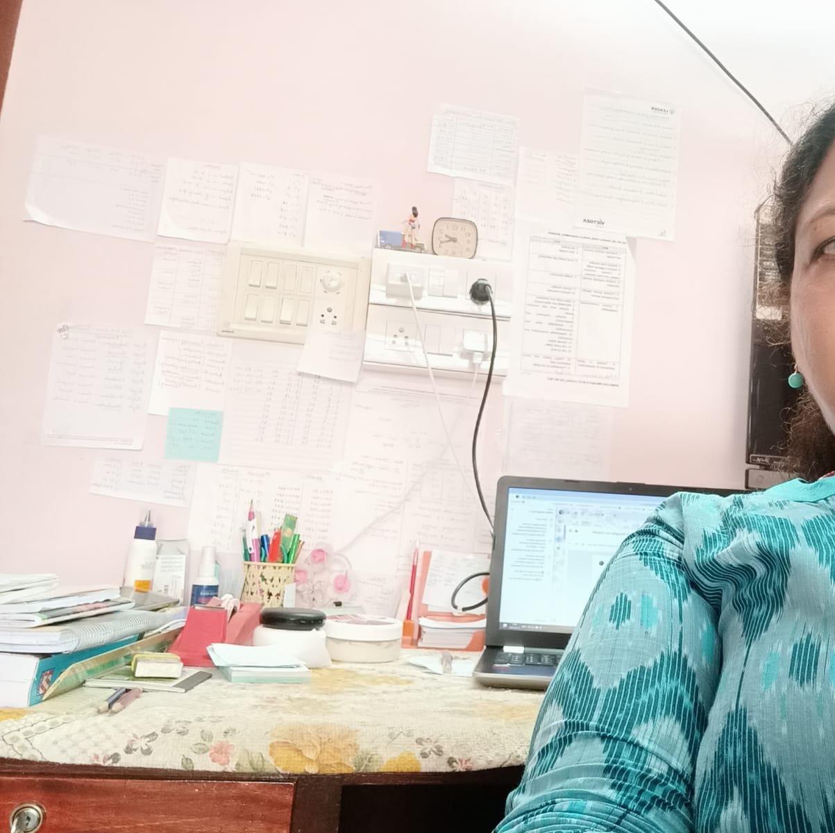 A work desk with a laptop and a wall of handwritten exam notes, a woman working from home towards financial independence
